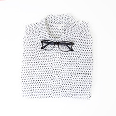 the glasses lie on the white neatly folded men`s shirt with a long sleeve instead of a bow tie