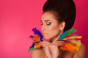 Pretty young woman on colorful background holding feathers. Portrait of attractive girl with creative make up