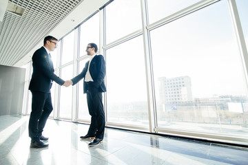 Full length side view of businessmen shaking hands in office windows.