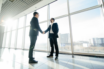 Full length side view of businessmen shaking hands in office windows.