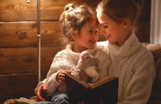  happy family mother and child daughter read a book on  winter evening