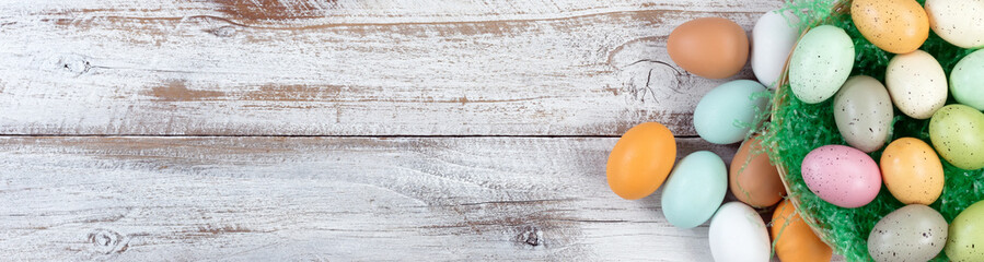 Top view of Easter eggs inside of basket with grass on white rustic wood