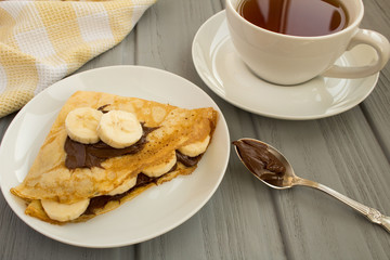 Breakfast: crepes with  banana ,chocolate and  tea  on the wooden  grey background