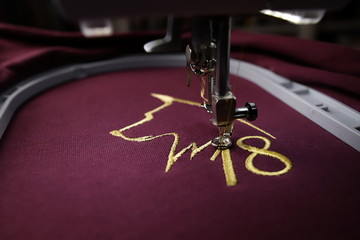 Embroidery with embroidery machine of dog silhouette and number 2018  in gold on claret fabric -...