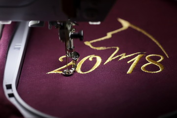 Embroidery with embroidery machine of dog silhouette and number 2018  in gold on claret fabric -...