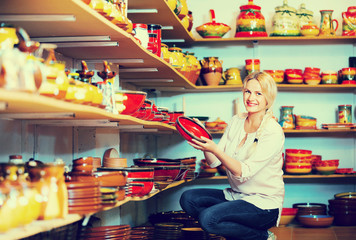 Portrait of glad woman choosing glazed with red color ceramic ut