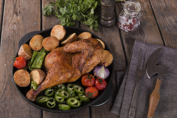fried chicken half with potatoes and tomatoes in the frying pan