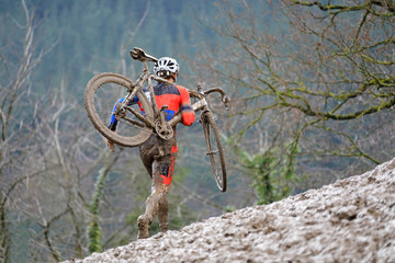 ciclocross competición ciclista con la bicicleta al hombro en pista de barro país vasco...