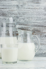 Milk in the glass jugs, white wooden background
