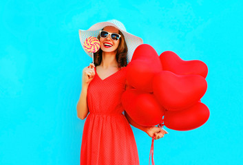 Happy laughing woman in hat with a lollipop candy, air balloons on blue background