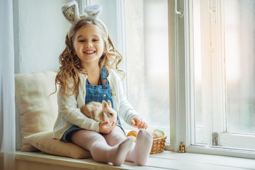 Cute happy little child girl is wearing bunny ears on Easter day holding little rabbit