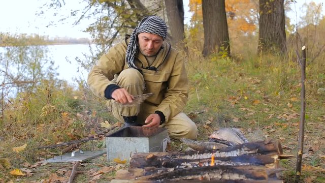 the man hunter puts the shavings of the trees in the smokehouse. Bonfire on the river bank.
