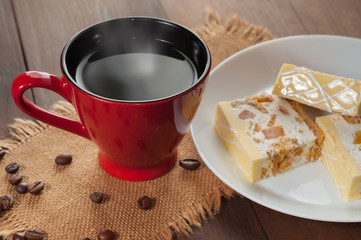 Red cup with coffee and lemon cake on a plate on sackcloth on a wooden table