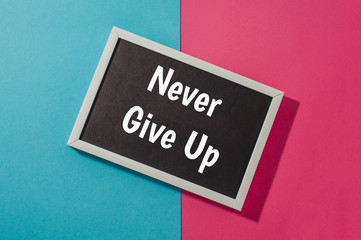 Never give up - text on chalkboard on blue and pink bright background.