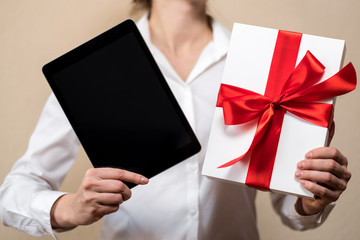 A woman in a white shirt is holding a gift, a black tablet and white gift box