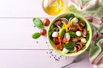 Fresh salad with spinach, bell peppers, tomatoes, red onions and mozzarella on purple wooden background.