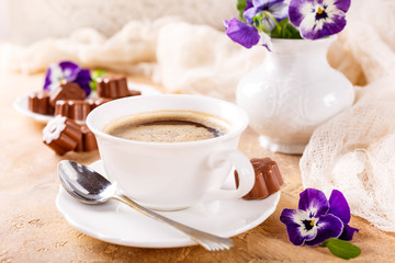Holiday food composition with cup of cooffee, chocolate candies in flower shape and violets. Postcard concept.