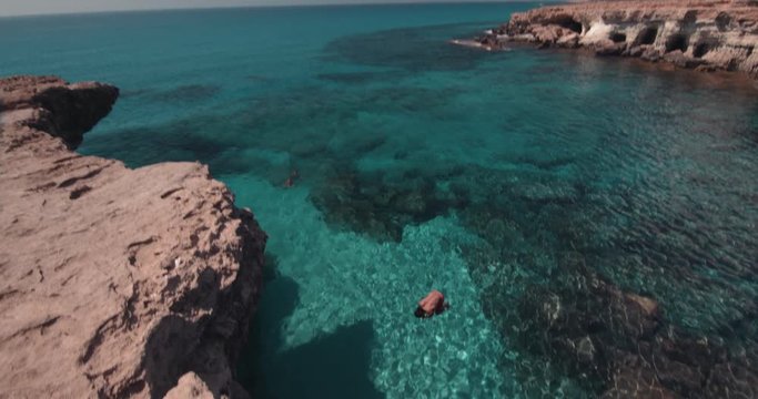 Young cliff diver jumping off rock into sea with somersault