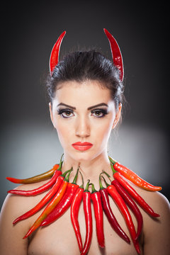 Beautiful young woman portrait with red hot and spicy peppers, fashion model with creative food vegetable make up looking side to empty copy space, isolated over black background. Red chili Paprika.