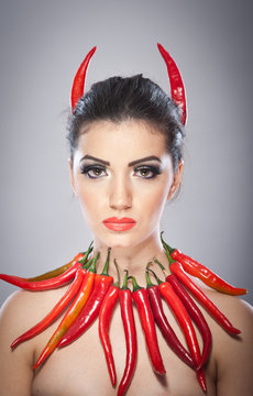 Beautiful young woman portrait with red hot and spicy peppers, fashion model with creative food vegetable make up looking side to empty copy space, isolated over black background. Red chili Paprika.