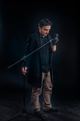 Young handsome man dressed casual with a microphone against a dark background 