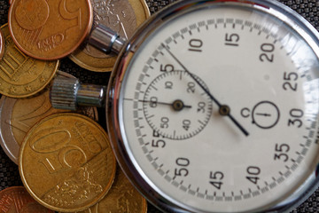 Pile of euro coins with old vintage stopwatch on brown jeans background