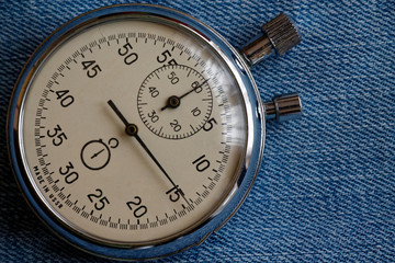 Stopwatch on worn blue jeans background, value measure time, old clock arrow minute and second accuracy timer record