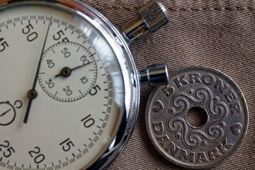 Denmark coin with a denomination of 5 krone (crown) and stopwatch on beige jeans backdrop - business background