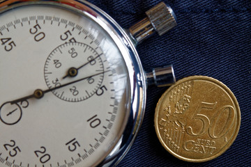 Euro coin with a denomination of 50 euro cents and stopwatch on obsolete blue denim backdrop - business background