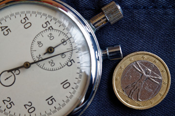 Euro coin with a denomination of one euro (back side) and stopwatch on worn blue jeans backdrop - business background