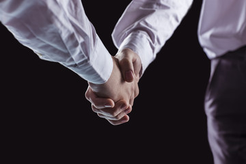 concept of a reliable partnership: a close-up of handshake of business partners on a black background.