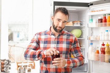 Handsome man opening jar near refrigerator in kitchen
