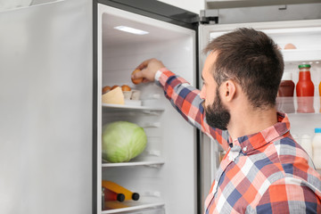 Handsome man choosing food in refrigerator at home