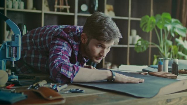 Craftsman working with leather at home workshop. Work with love. Worker checking quality of leather material. Handsome man touching piece of leather lying on table at workshop