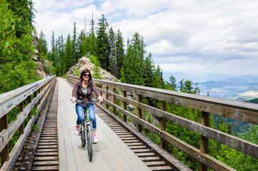 Naklejka premium Woman Riding a Bicycle across a Wooden Bridge along a Mountain Path on a Spring Day.