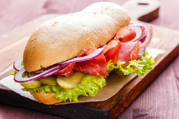 Sandwich with ham, onion, lettuce and pickles on a wooden cutting board close-up