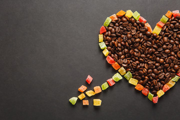 Candied fruits in the form of heart with arrow, brown coffee beans isolated on black background for design. Saint Valentine's Day card on fabruary 14, holiday concept. Copy space for advertisement.