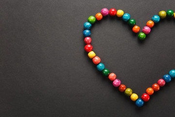 Colorful wooden beads in the form of heart isolated on black background for design. Saint Valentine's Day card on fabruary 14, holiday concept. Copy space for advertisement.