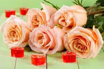 five beige rose with candles in the shape of heart on a green wooden background