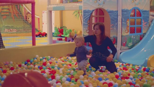 Mom and blond toddler have fun in dry pool with little balls