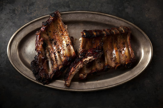 Grilled pork spare ribs cooked with balsamic vinegar and honey sauce on vintage metallic tray. Dark rustic background.