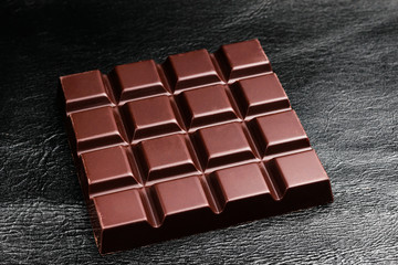 Dark, bitter chocolate bar on black leather texture background