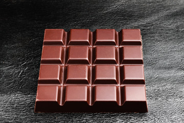 Dark, bitter chocolate bar on black leather texture background