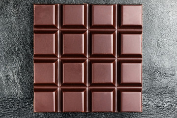 Dark, bitter chocolate bar on black leather texture background, top view