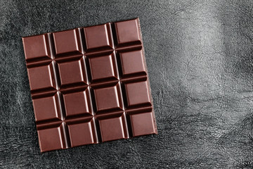 Dark, bitter chocolate bar on black leather texture background, top view