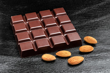 Dark, bitter chocolate bar and almond nuts on black leather texture background