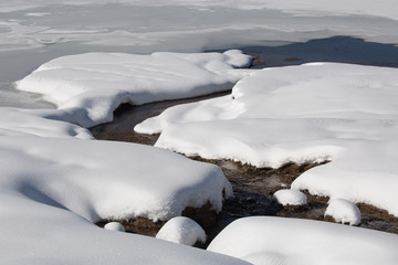 A small stream zigzags through a snow covered field into a frozen lake