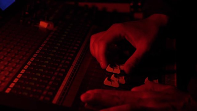 Manos ajustando niveles en mesa de control de audio en concierto de musica y luces en color rojo