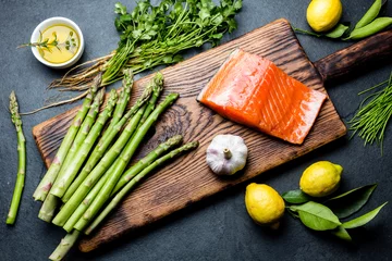 Papier Peint photo autocollant Plats de repas Ingredients for cooking. Raw salmon fillet, asparagus and herbs on wooden board. Food cooking background with copy space. Top view.