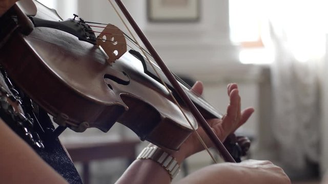 unrecognizable woman holds fiddlestick in hand and play on a violin close-up indoors